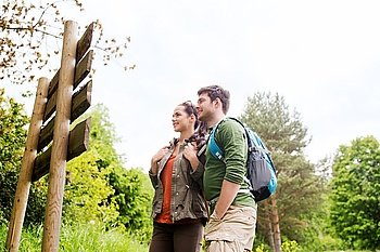 adventure, travel, tourism, hike and people concept - smiling couple with backpacks standing at signpost outdoors