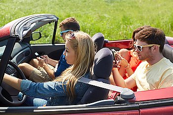 leisure, road trip, travel and people concept - friends with smartphones driving in cabriolet car along country road