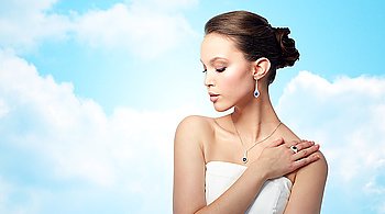 beauty, jewelry, people and luxury concept - beautiful asian woman or bride with earring, finger ring and pendant over blue sky and clouds background