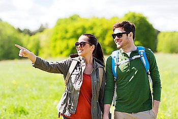 travel, hiking, backpacking, tourism and people concept - happy couple with backpacks walking outdoors and pointing finger to something