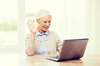 technology, age, gesture, communication and people concept - happy senior woman with laptop computer having video chat at home and waving hand