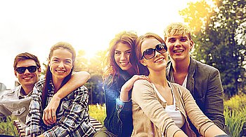 summer holidays, friendship, leisure and teenage concept - group of students or teenagers hanging out and hugging at campus or park
