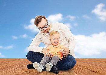 family, childhood, fatherhood, leisure and people concept - happy father and and little son over blue sky and wooden floor background