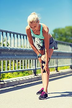fitness, sport, exercising and healthy lifestyle concept - young woman with injured knee or leg outdoors