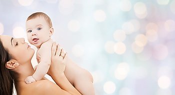 family, motherhood, parenting, people and child care concept - happy mother holding adorable baby over blue holidays lights background