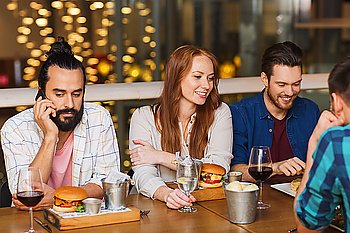 leisure, technology, lifestyle and people concept - man with smartphone and friends dining at restaurant