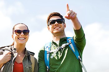 travel, hiking, backpacking, tourism and people concept - happy couple with backpacks outdoors pointing finger to something over sky