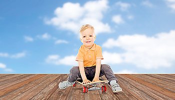 childhood, sport, leisure and people concept - happy little boy sitting on skateboard over blue sky and clouds background