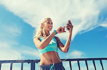 fitness, sport, people, technology and healthy lifestyle concept - smiling young woman with smartphone and earphones listening to music and exercising outdoors