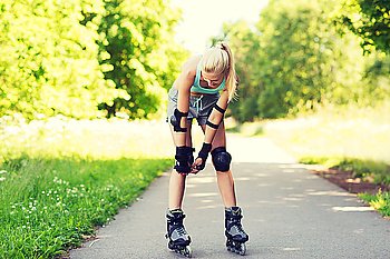 fitness, sport, summer, rollerskating and healthy lifestyle concept - happy young woman in rollerskates and protective gear riding outdoors