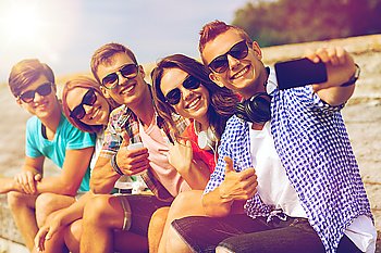 friendship, summer, technology, gesture and people concept - group of smiling friends with smartphone and headphones making selfie outdoors