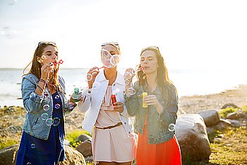 summer vacation, holidays, fun and people concept - group of happy young women or teenage girls blowing bubbles on beach
