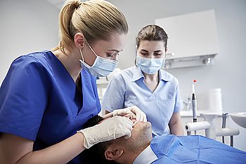 people, medicine, stomatology and teeth care concept - female dentist with assistant checking male patient dental occlusion teeth at dental clinic office