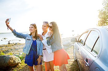 summer vacation, holidays, travel, road trip and people concept - happy teenage girls or young women with smartphone taking selfie near car at seaside