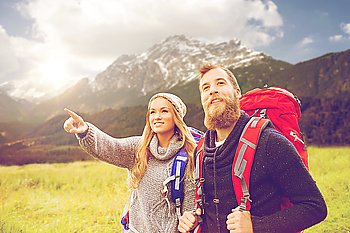 adventure, travel, tourism, hike and people concept - smiling couple walking with backpacks over alpine mountains and hills background