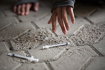 substance abuse, addiction, people and drug use concept - close up of addict woman hands and used syringes on ground