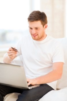 smiling man with laptop and credit card at home