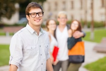 summer holidays, education, campus and teenage concept - smiling teenage boy in eyeglasses with classmates on the back