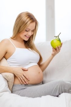 pregnancy, motherhood, healthcare, food and happiness concept - happy pregnant woman sitting on sofa with fresh green apple