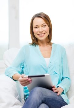 home, technology and internet concept - smiling woman sitting on the couch with tablet pc at home