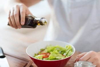 cooking and home concept - close up of male hands flavouring salad in a bowl with olive oil