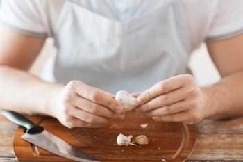 cooking and home concept - close up of male hands taking off peel of garlic on cutting board