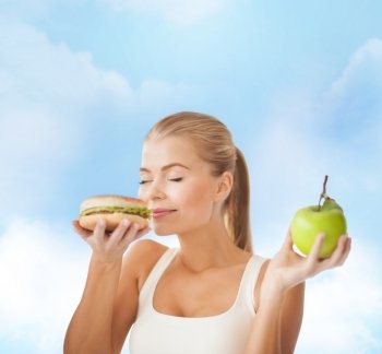 health, diet and food concept - happy woman smelling hamburger and holding apple