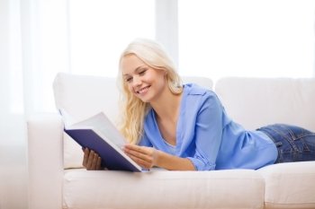 leasure and home concept - smiling woman reading book and lying on couch at home