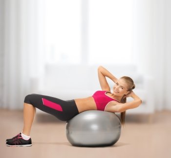 fitness, gym, exercise and health concept - young woman doing exercise on fitness ball at home