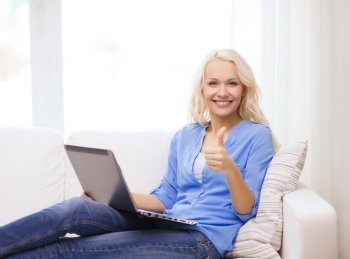 home, technology, gesture and internet concept - smiling woman sitting on the couch with laptop computer at home showing thumbs up