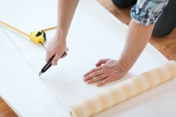 repair, building and home concept - close up of male hands cutting wallpaper