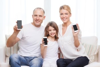 family, child, technology and home concept - smiling parents and little girl with blank black screen smartphones at home