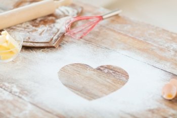 cooking and love concept - close up of heart of flour on wooden table at home