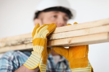 repair, building and home concept - close up of male in gloves and helmet carrying wooden boards on shoulder