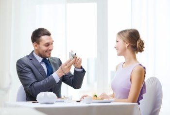 restaurant, couple, technology and holiday concept - smiling man taking picture of wife or girlfriend with digital camera at restaurant