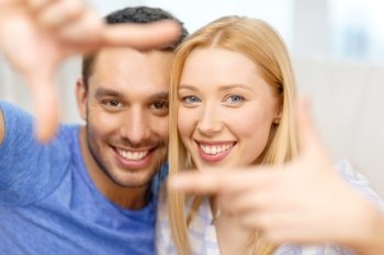 love, family and happiness concept - smiling happy couple making frame gesture at home