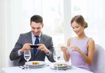 restaurant, couple, technology and holiday concept - smiling couple taking picture of appertizer with smartphone camera at restaurant
