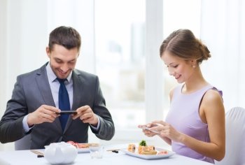restaurant, couple, technology and holiday concept - smiling couple taking picture of sushi with smartphone camera at restaurant