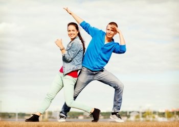 summer holidays, teenage and dancing concept - couple of teenagers dancing outside