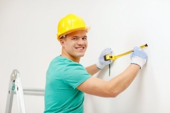 repair, building and home concept - smiling man in yellow protective helmet measuring wall