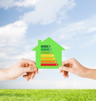energy saving, real estate and family home concept - closeup of couple hands holding green paper house with energy efficiency rating
