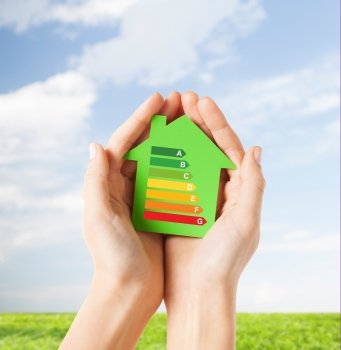 energy saving, real estate and family home concept - closeup of female hands holding green paper house with energy efficiency rating