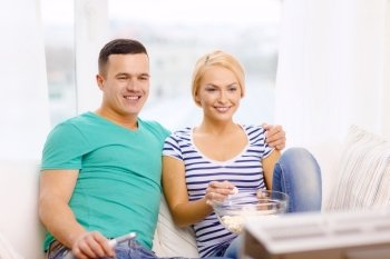 food, love, family and happiness concept - smiling couple with popcorn watching movie at home