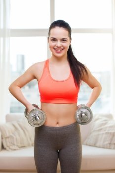 fitness, home and diet concept - smiling girl exercising with heavy dumbbells at home