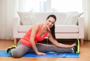 fitness, home, technology and diet concept - smiling teenage girl streching on floor with smartphone and earphones at home