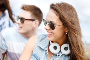 summer holidays, people and happiness concept - smiling teenage girl in sunglasses outdoors with friends