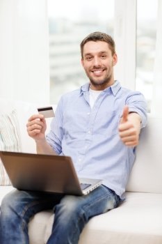 technology, home and lifestyle concept - smiling man working with laptop and credit card at home and showing thumbs up