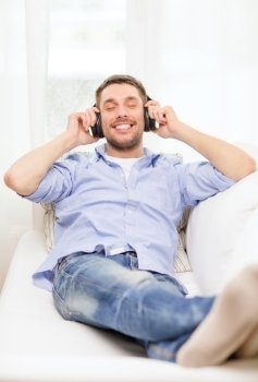 technology, music and happiness concept - smiling young man in headphones at home