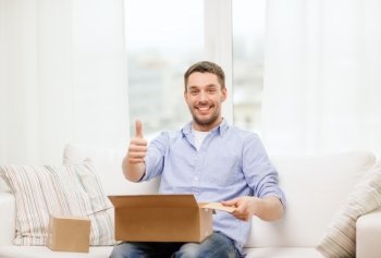 post, home and lifestyle concept - smiling man with cardboard boxes at home showing thumbs up
