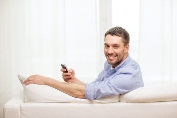 home, technology and internet concept - smiling man with smartphone sitting on couch at home